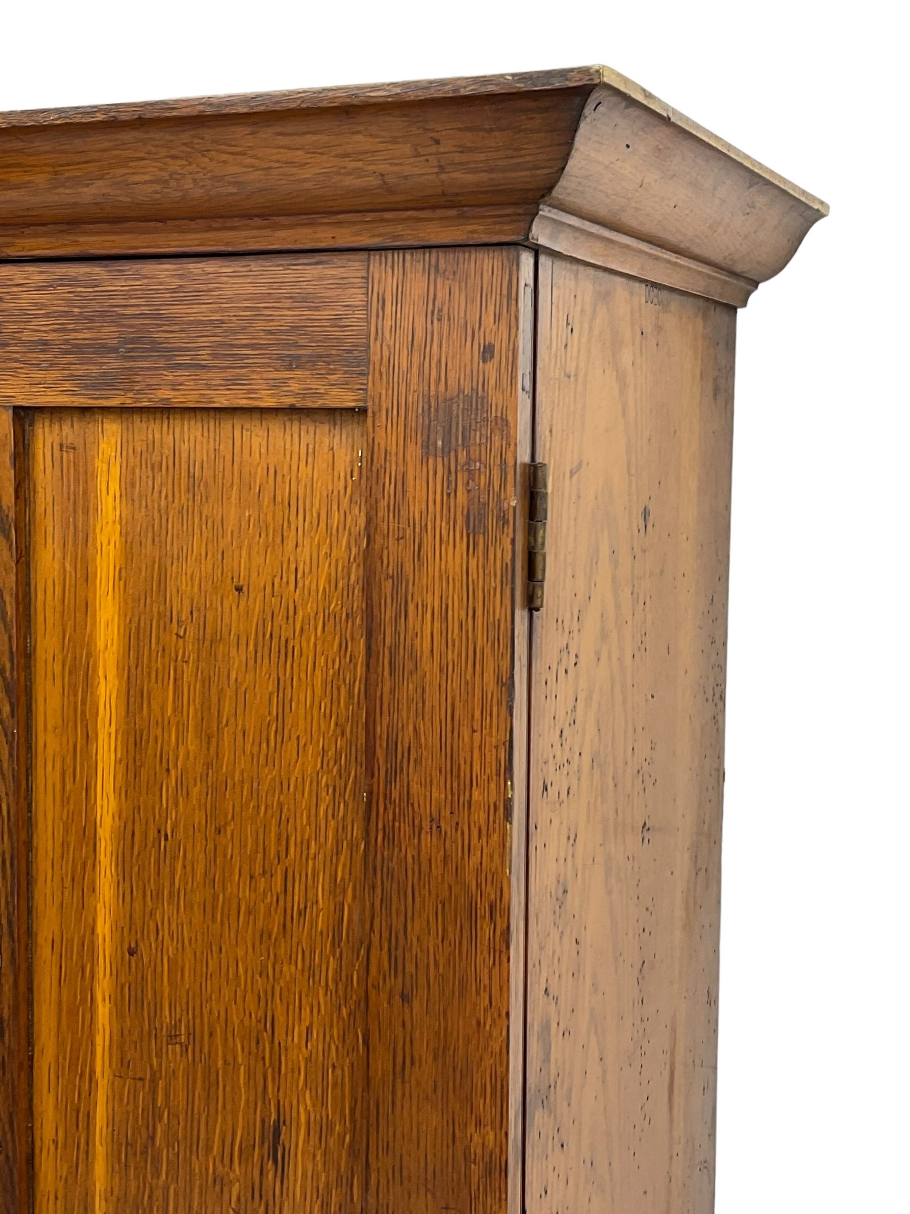 The North of England School Furnishing Company Limited Darlington - early 20th century oak school cupboard, projecting moulded cornice over two panelled doors, fitted with shelves, on chamfered plinth base 