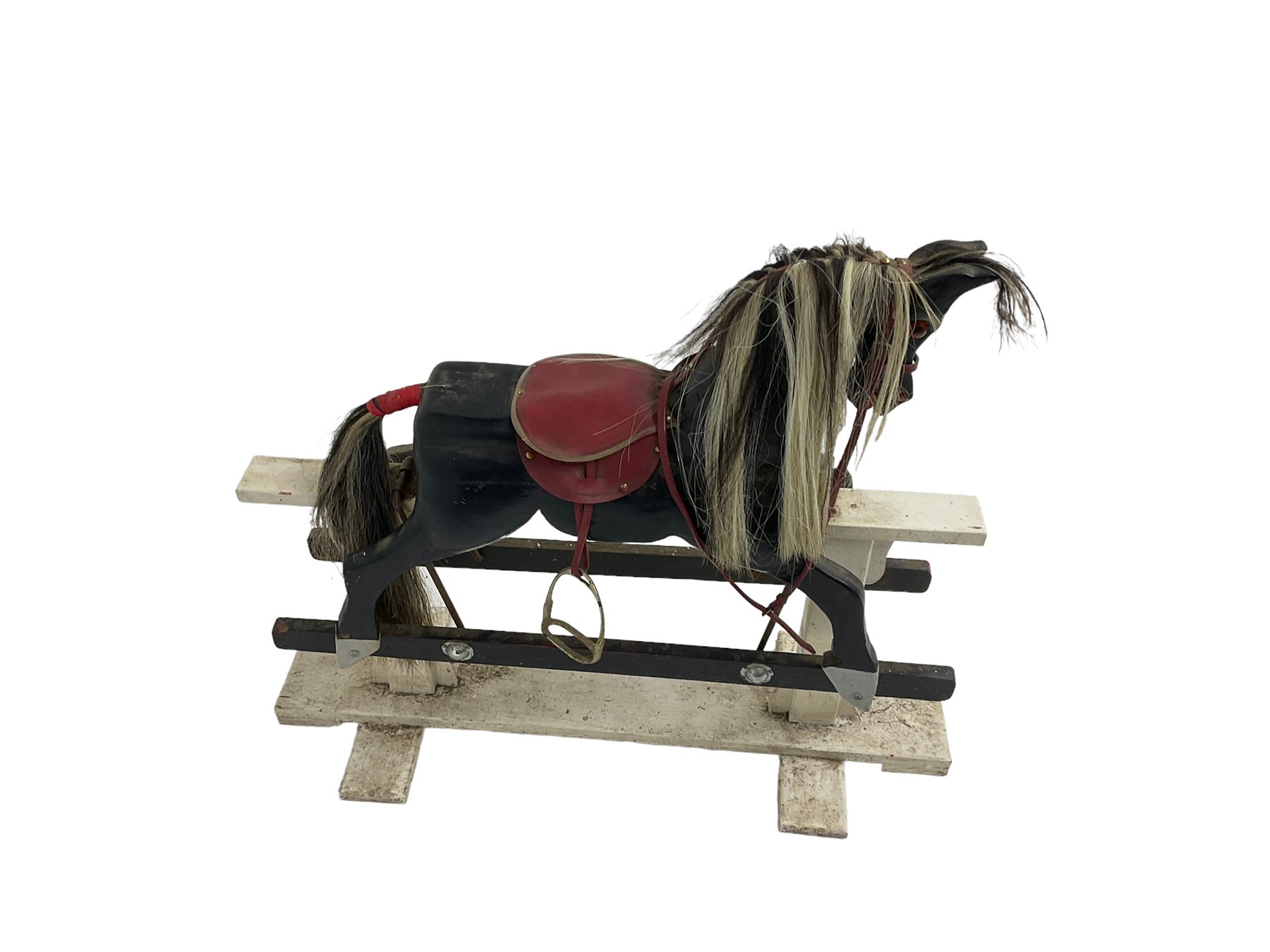 20th century black painted rocking horse on white painted trestle base, fitted with saddle and stirrups 
