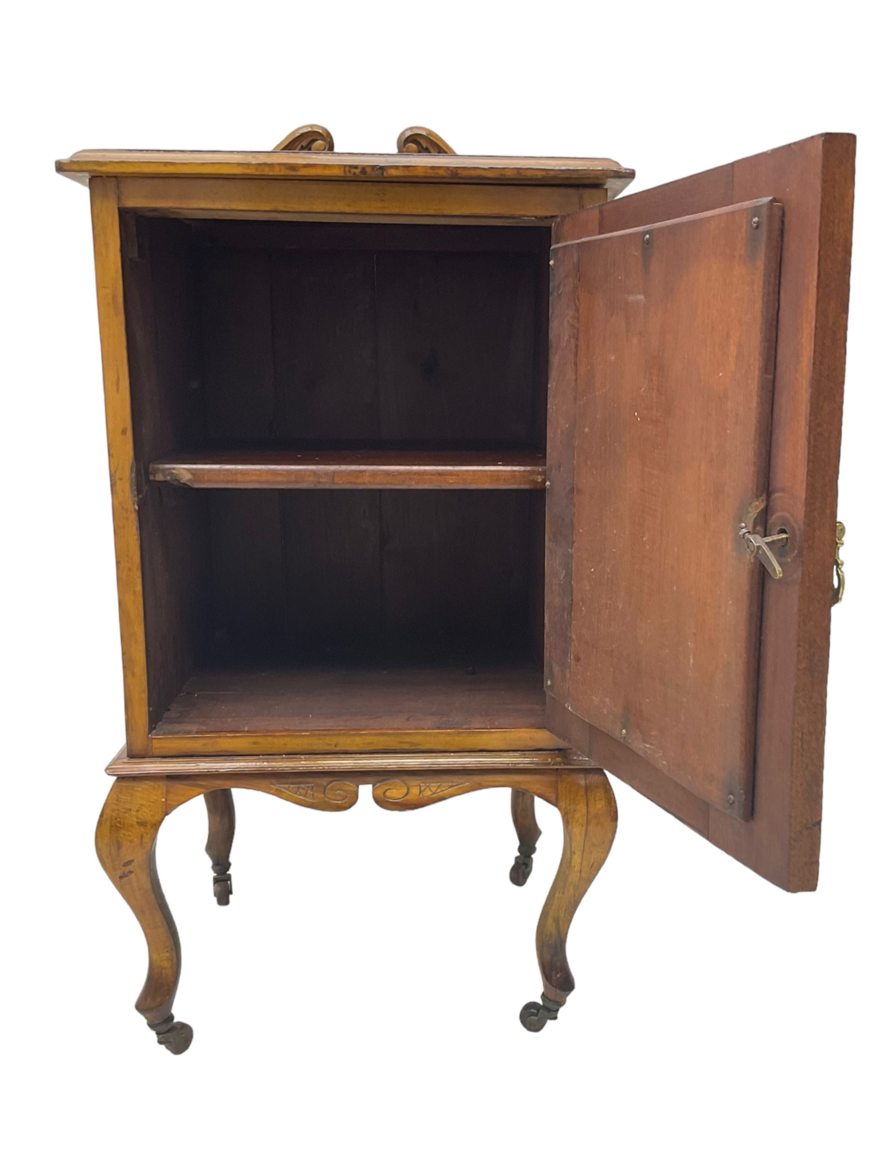 Edwardian Art Nouveau walnut bedside cabinet, raised broken swan neck back with carved flower heads, single fielded panelled door enclosing single shelf, raised on cabriole supports with ceramic castors