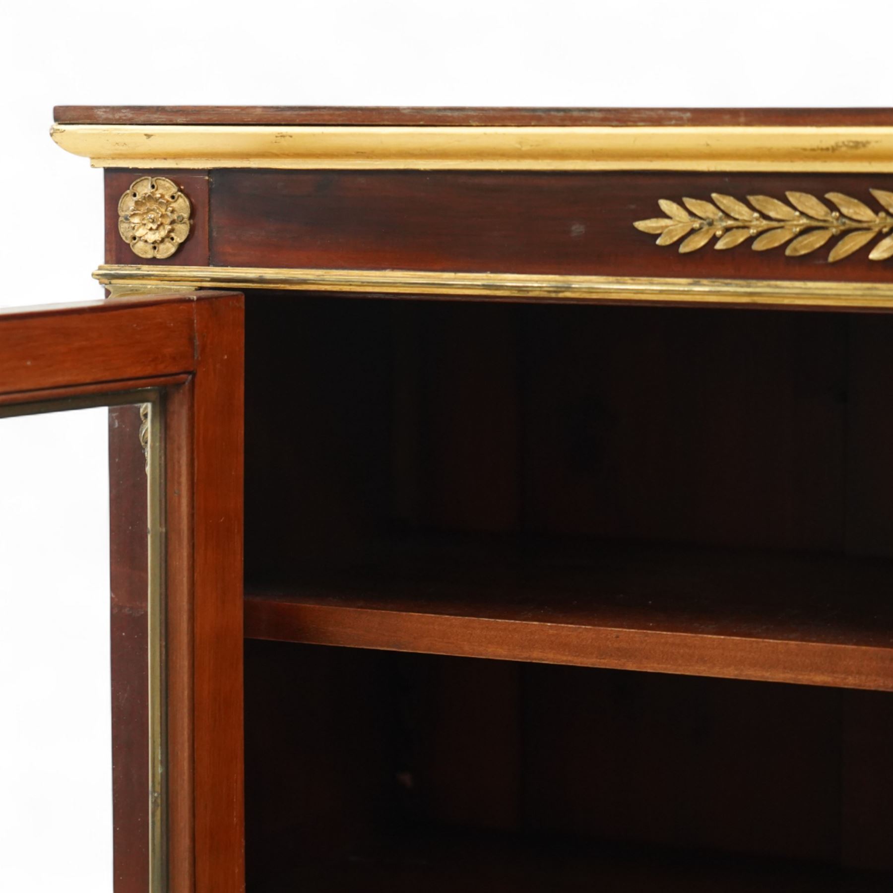 19th-century French Empire-style mahogany and gilt bronze-mounted glazed cabinet, rectangular top above frieze with applied gilt bronze laurel swags and rosettes with gilt brass borders, over two glazed panel doors enclosing three adjustable shelves, flanked by plain pilasters with applied mounts, raised on gilt bronze paw feet 