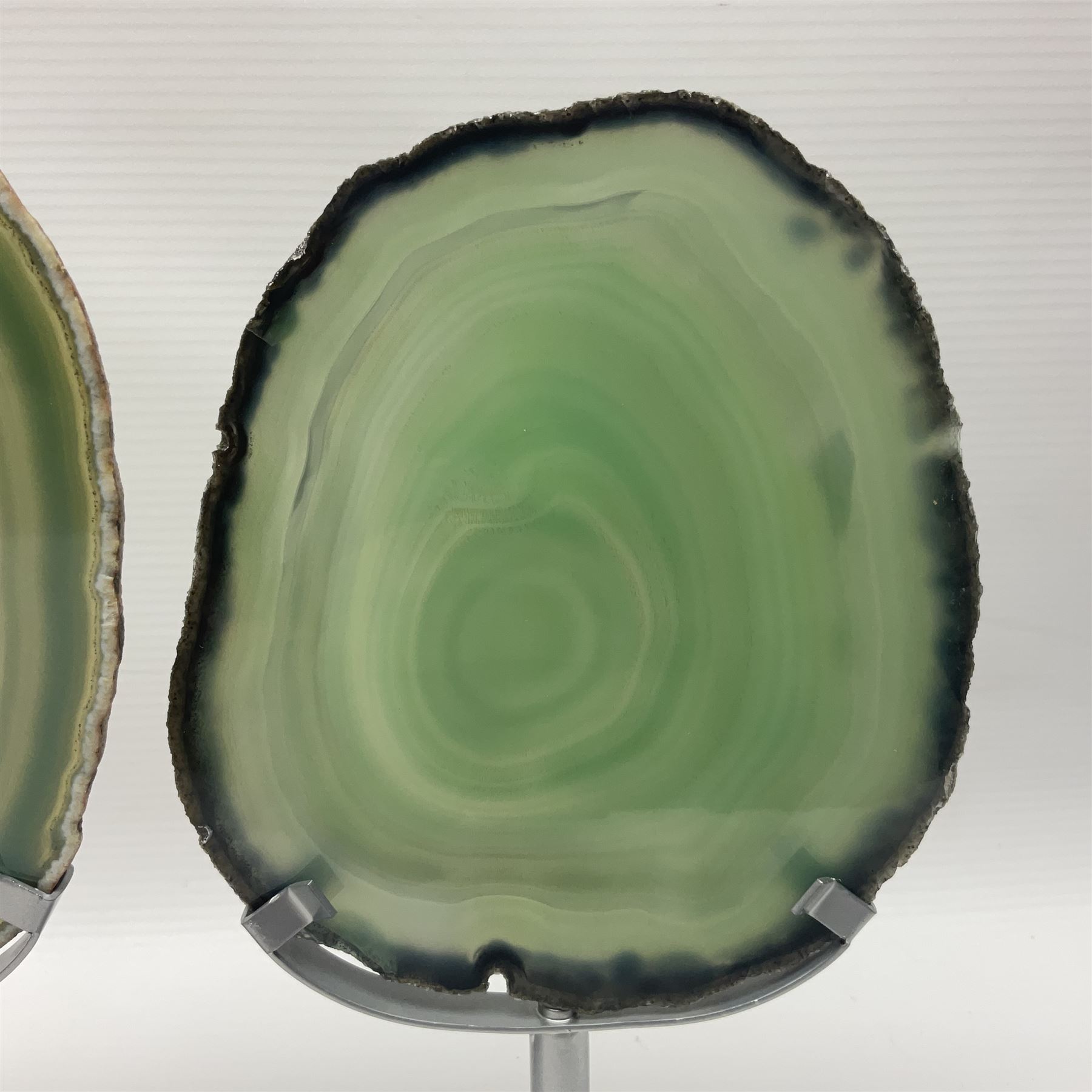 Pair of green agate slices, polished with rough edges raised upon silvered metal stands, H19cm