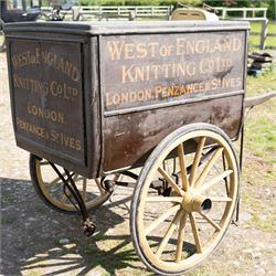 West of England Knitting Co. Ltd. Advertising Hand Cart

A rare and highly decorative late Victorian or Edwardian advertising hand cart, retaining its original black painted finish and gilt signwriting for West of England Knitting Co. Ltd., London, Penzance & St Ives. The enclosed box body is mounted on large cream painted wooden spoked wheels and fitted with rear push handles, allowing the cart to be manoeuvred by hand. Intended as a promotional and delivery vehicle for one of Britain's best known knitwear manufacturers, the cart survives as an evocative piece of commercial advertising history. The interior remains accessible via twin rear doors, while traces of the original maker's transfer for the Warwick Carrier are visible. An unusual and attractive display piece suited to collectors of advertising, transport memorabilia and social history.

Features

• Original hand painted gilt signwriting for West of England Knitting Co. Ltd.
• Advertising panels referencing London, Penzance and St Ives
• Enclosed wooden box body with twin rear access doors
• Original black painted finish with period lettering
• Large cream painted wooden spoked wheels with iron tyres
• Rear push handles for hand propelled operation
• Warwick Carrier maker's transfer remains visible
• Original undercarriage and running gear
• Attractive display piece with strong commercial advertising appeal
• Suitable for museum, retail, interior or collection display

Dimensions:
Overall length: 190 cm
Body length: 125 cm
Overall width: 140 cm
Body width: 100 cm
Height: 150 cm

Wheel Diameter:
Wheels: 92 cm