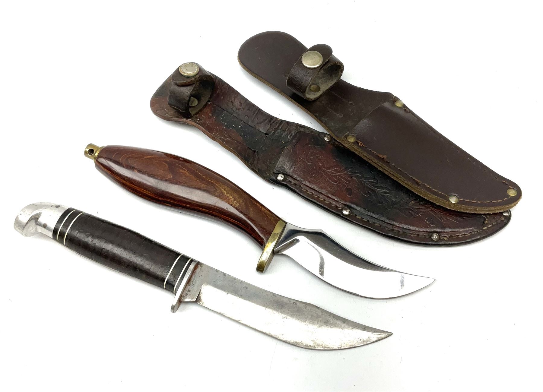 Western Boulder Colorado hunting knife the 11.5cm curving blade with maker's name to the ricassso, leather strip bound grip and aluminium pommel, in oak leaf decorated leather sheath L24cm; and J. Adams Sheffield hunting knife with curving blade and laminated wooden grip, in leather sheath (2)