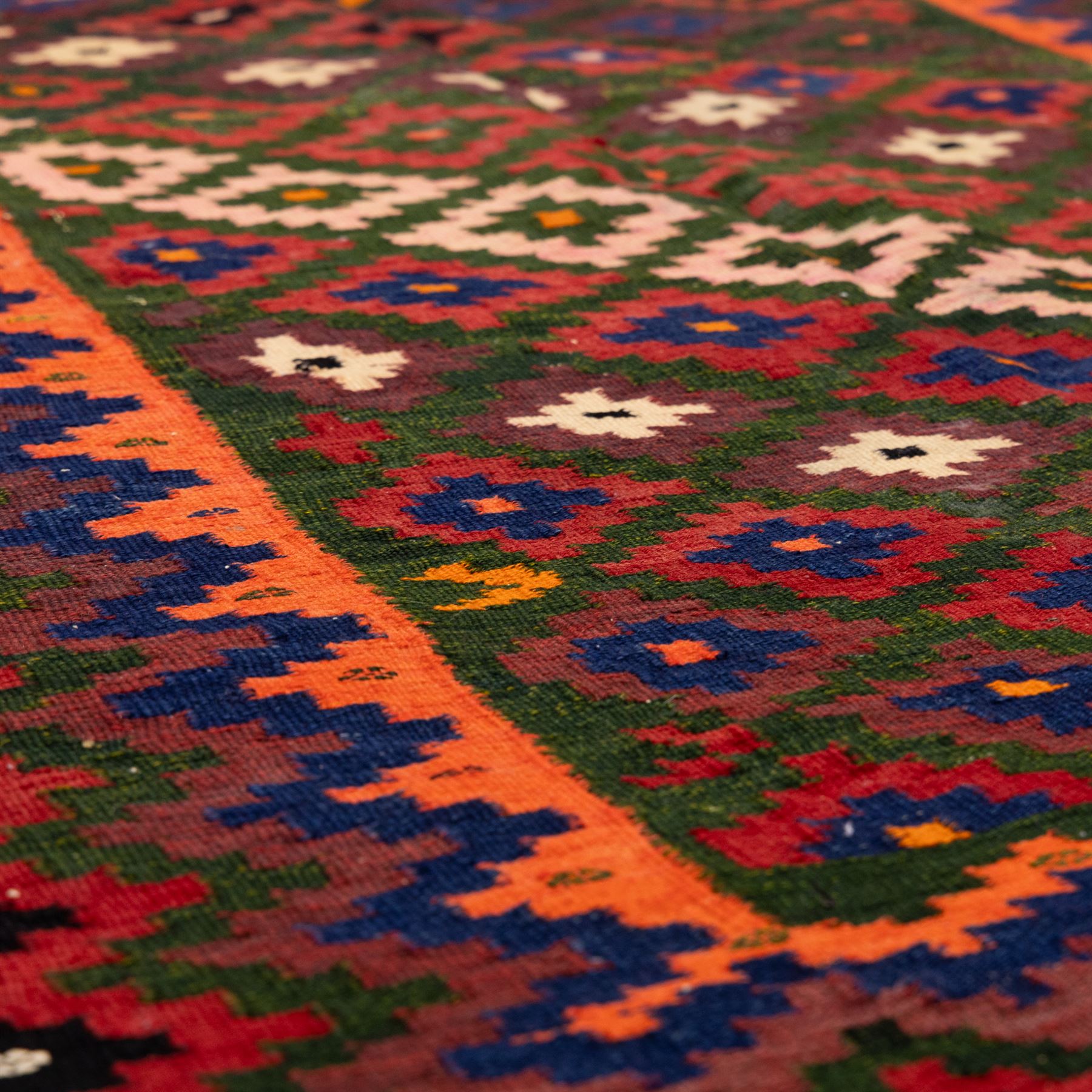 North East Persian Sumak flatweave kilim, woven with an all-over arrangement of stepped diamond motifs, including a diagonal band of contrasting colours in shades of red, indigo, green, pink, and ivory, framed by multiple geometric borders incorporating serrated chevron designs  