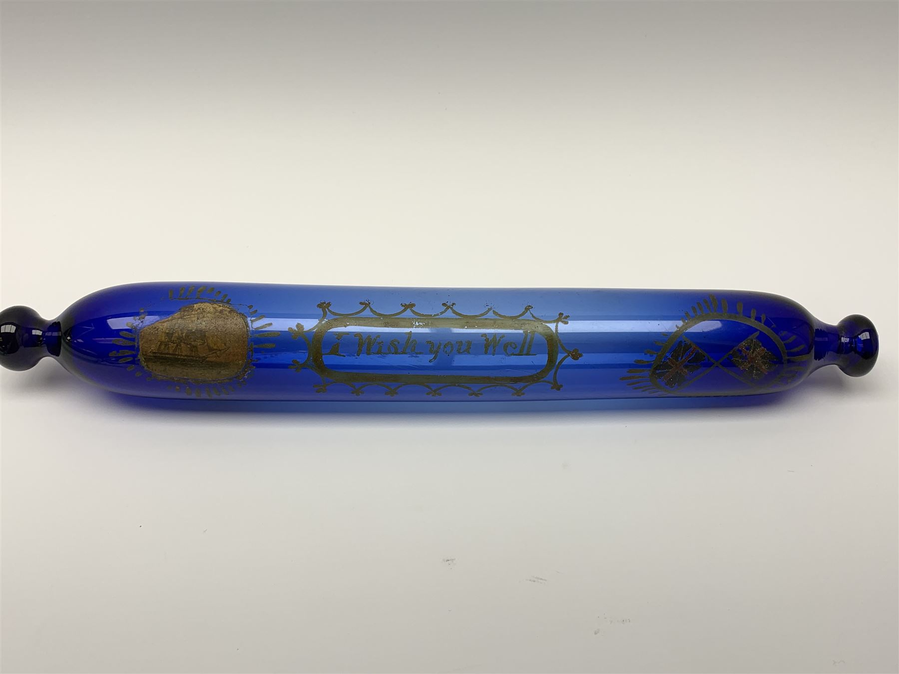 19th century Bristol blue glass rolling pin, with printed and gilt decoration of a schooner, crossed union flags, and inscription 'I wish you well', L36cm, together with another 19th century green glass example, L39cm