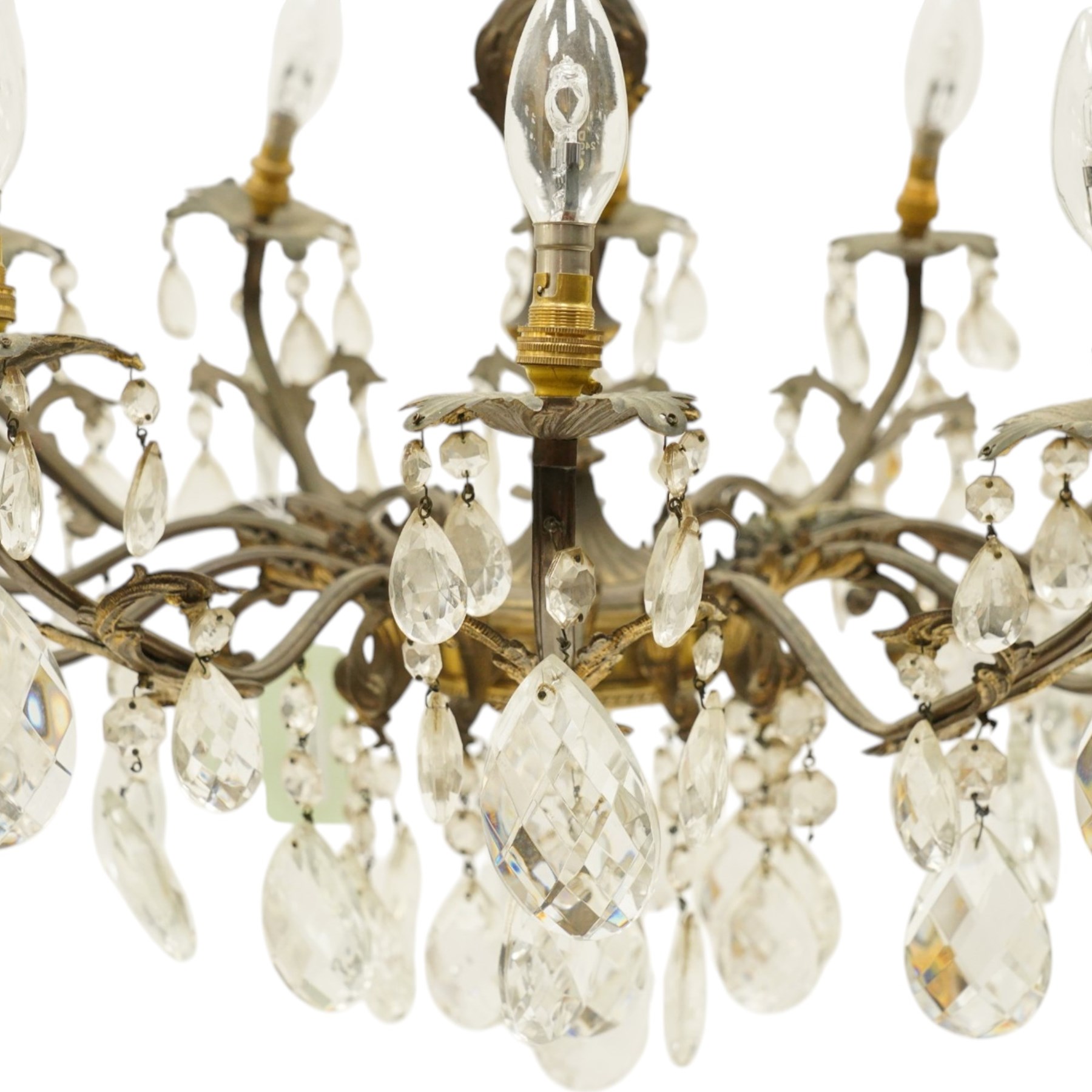 20th century Louis XV design gilt and patinated metal twelve-light chandelier, the foliate-cast baluster stem issuing scrolling acanthus branches with leaf-form drip pans, hung throughout with faceted glass pendants and lustre drops, suspended from chains beneath a foliate ceiling rose