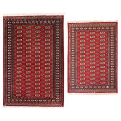 Two Afghan Bokhara crimson ground rugs, the fields decorated with repeating Gul motifs wit...