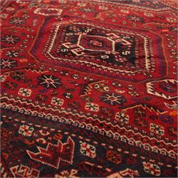 South West Persian Qashqai hand-knotted rug, madder red field with a large stepped diamond medallion with scattered geometric devices and indigo spandrels filled with geometric motifs, framed by multiple narrow guard borders and broad main border, wool fringe ends 