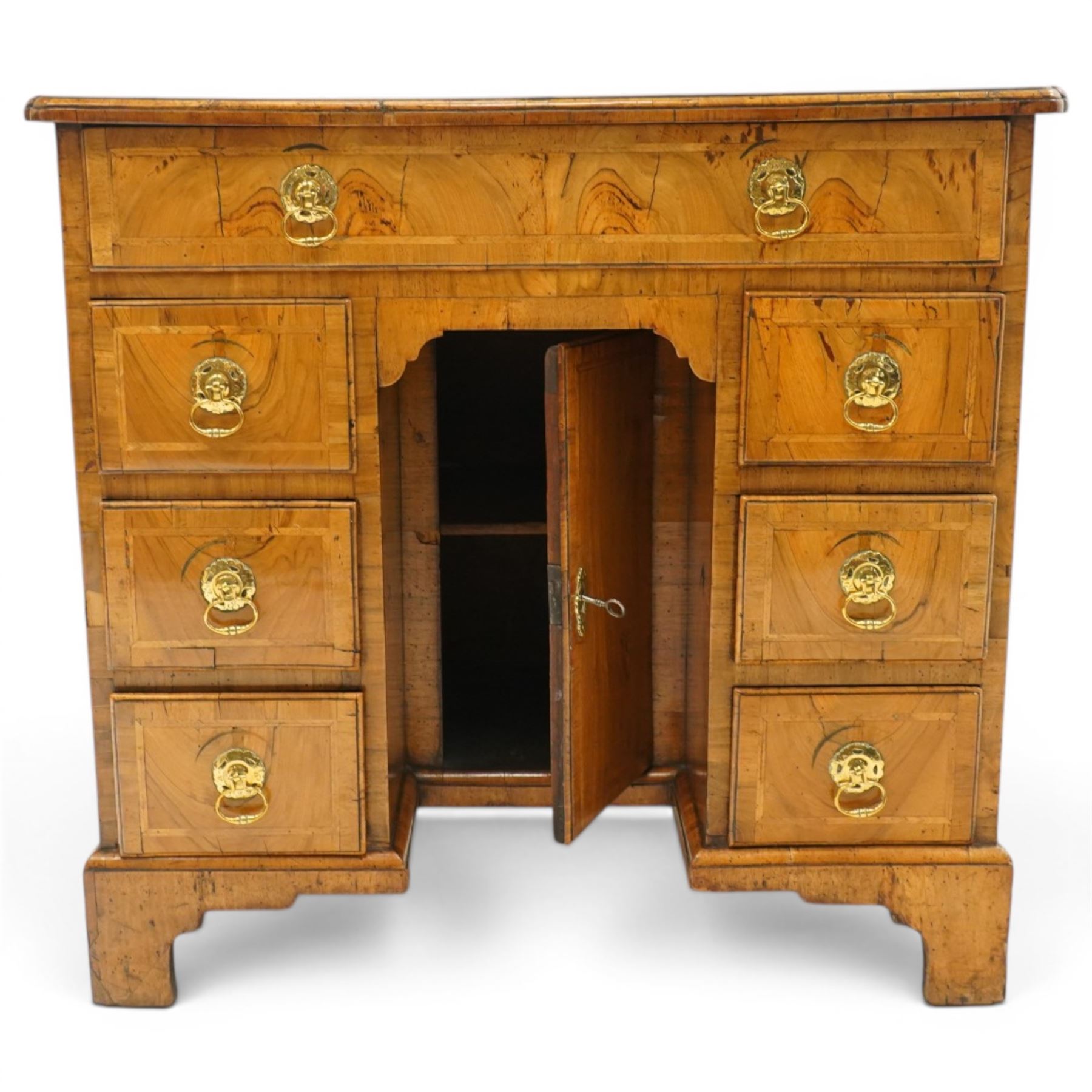 George III figured and burr walnut kneehole desk, the shaped rectangular top with feather and crossbanding surrounded by a moulded edge, fitted with single frieze drawer over three graduating drawers to each side, flanking a central recessed cupboard, lower moulded edge on bracket feet
Provenance: Kirkham Hall