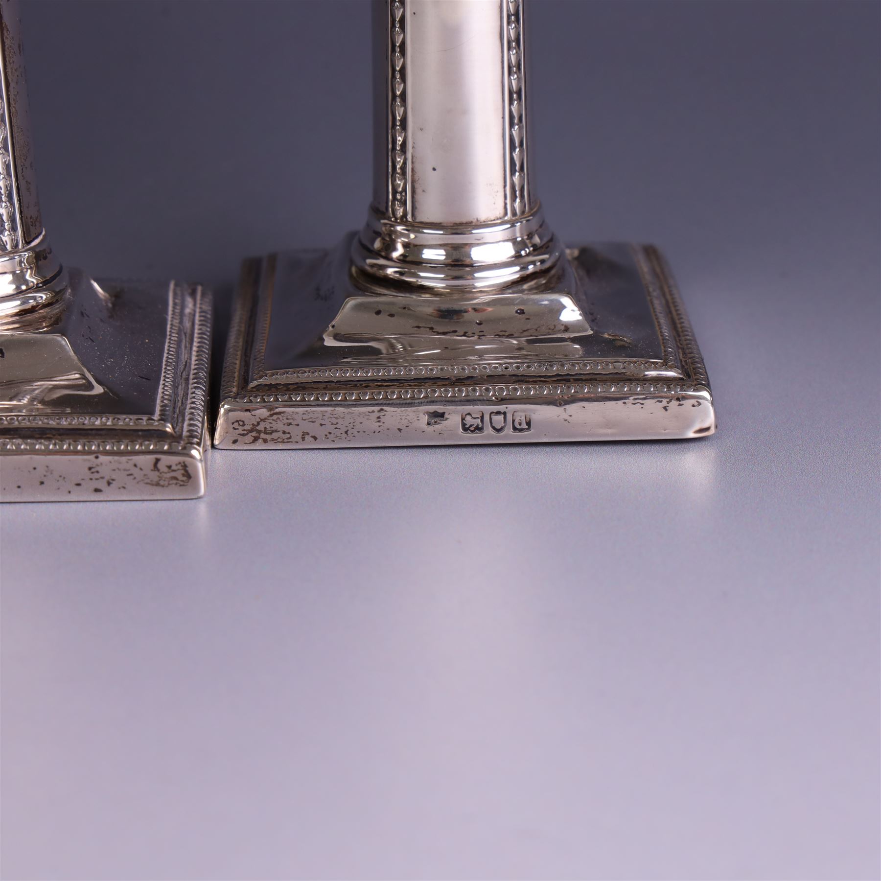 Pair of late Victorian silver mounted candlesticks, the stems embossed with classical ribbon and swag design, upon weighted stepped square bases, hallmarked London 1899, maker's mark worn and indistinct, H12cm