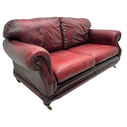 Thomas Lloyd - three-piece lounge suite, comprising of traditional shape two seat sofa (W190cm H80cm) and a pair of wingback armchairs (W100cm H91cm), each with rolled arms over turned supports with brass castors, upholstered in oxblood red leather