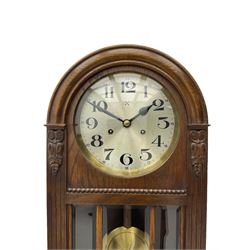 German HAC “ting tang” quarter striking wall clock in a round arched oak case with applied carving and beadwork, glazed door with a visible pendulum and silvered 24-hour dial with Arabic numerals and steel spade hands,  8-day spring driven movement striking on gong rods.

