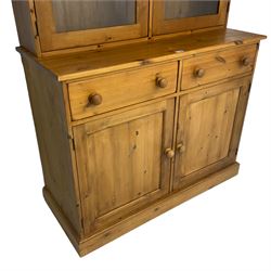 Large pine bookcase on cupboard, the upper section enclosed by two glazed door, the lower section fitted with two drawers and double cupboard, on plinth base