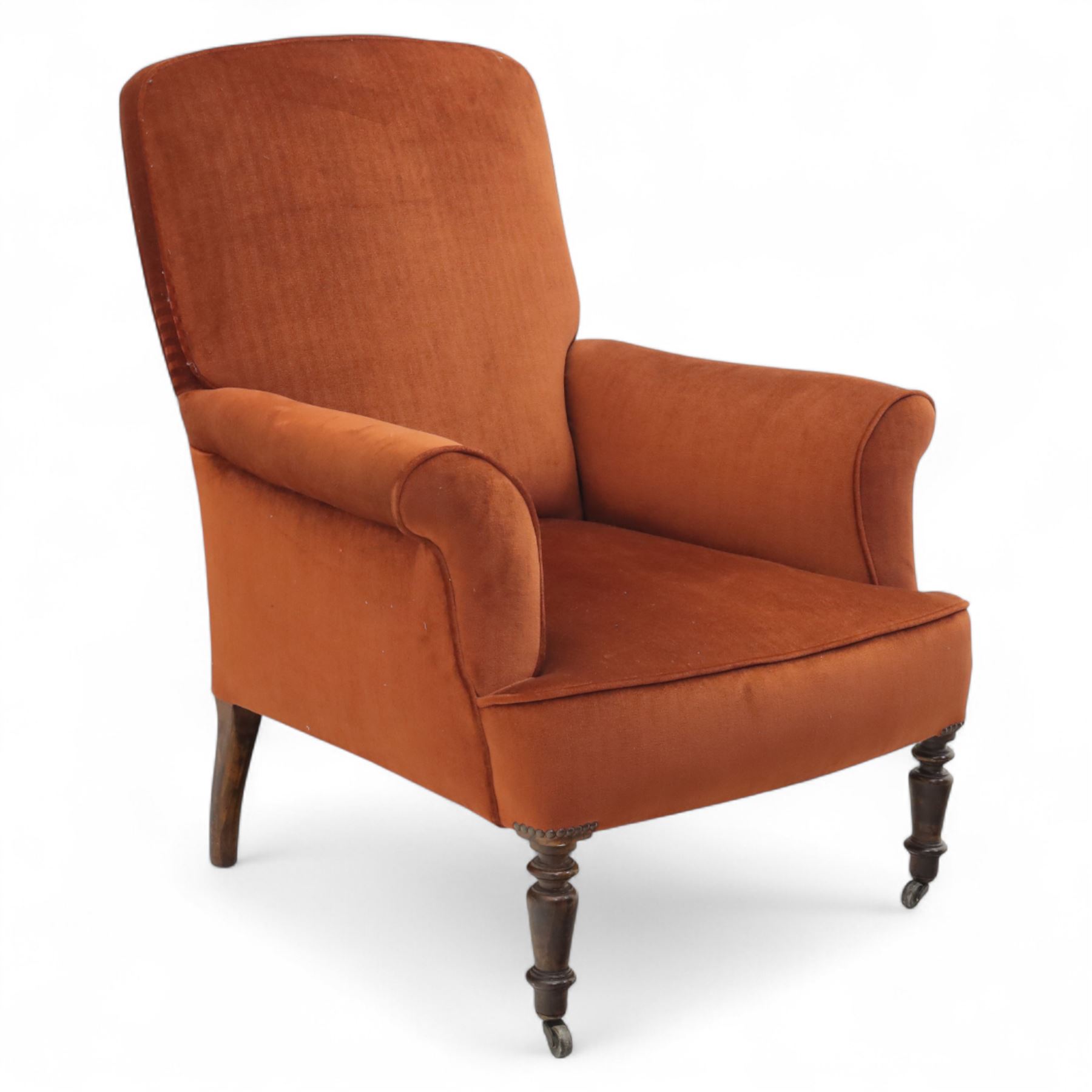 Late 19th century mahogany framed armchair, of generous proportion, upholstered in rust coloured velvet, with shaped back and scroll arms, raised on turned front legs with brass castors