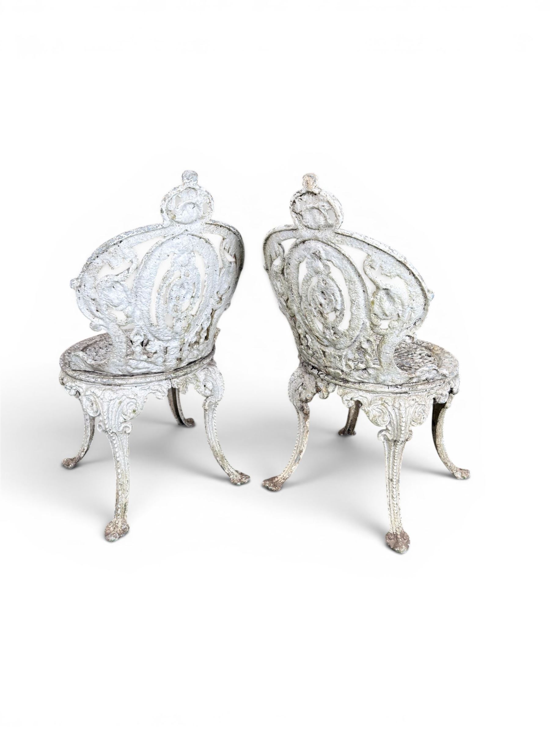 Pair of white painted cast metal garden chairs, ornate reclined backs, circular pierced seats on cabriole legs