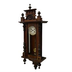 A late 19th century German wall clock with an 8-day spring driven movement striking the hours on a coiled gong, in a mahogany case with a shaped pediment and turned columns flanking a full-length glazed door, with a two-part dial enamel with Roman numerals, minute track and pierced gothic designed hands, gridiron pendulum and beat plate. With Key.




