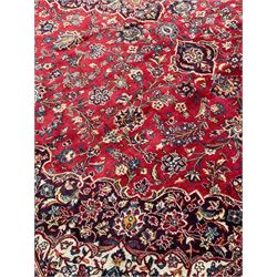 Large Persian Kashan crimson ground carpet, large floral central medallion surrounded by trailing branches decorated with leaves and stylised plant motifs, the main border with scrolling design interspersed with palmettes, within floral pattern guard stripes 