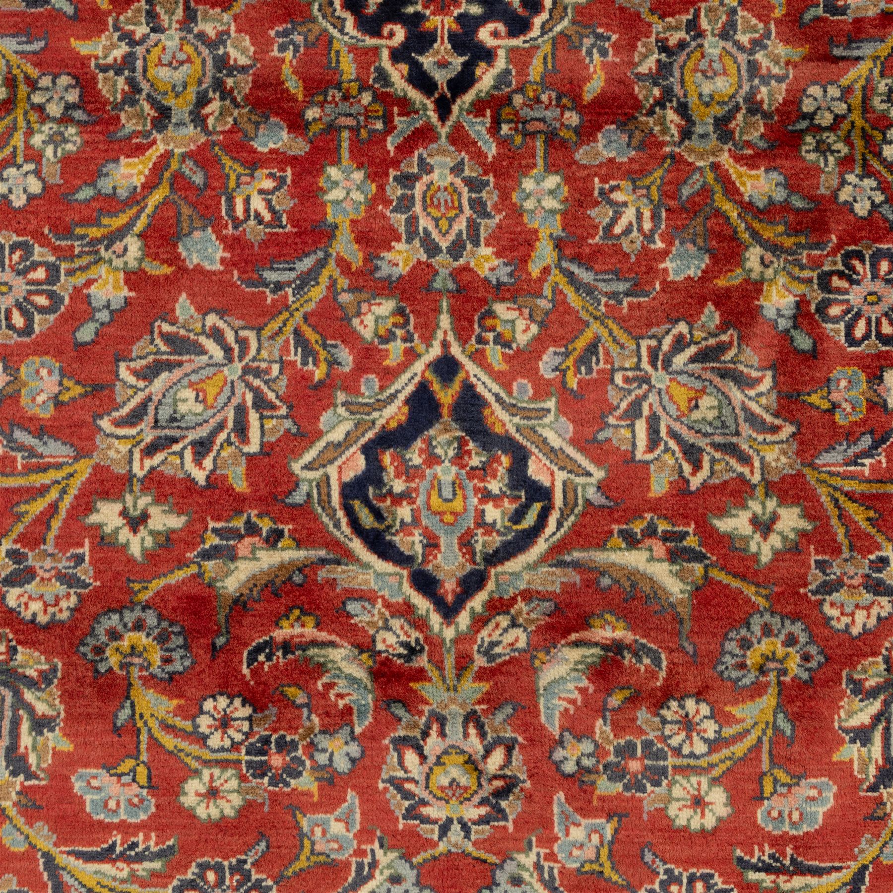 Persian Kashan carpet, the field in rich rust tone centred by an ivory and blue medallion with palmette extensions, surrounded by intricate foliate arabesques and stylised blooms, within triple floral borders incorporating palmettes and interlaced tendrils, woven in the region of Kashan