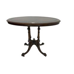Late 19th century oval walnut tilt-top loo table, figured quarter matched veneer with ebonised banding and foliate decoration, raised on platform base supported by four quadruple turned and fluted pillars, splayed carved supports with brass castors