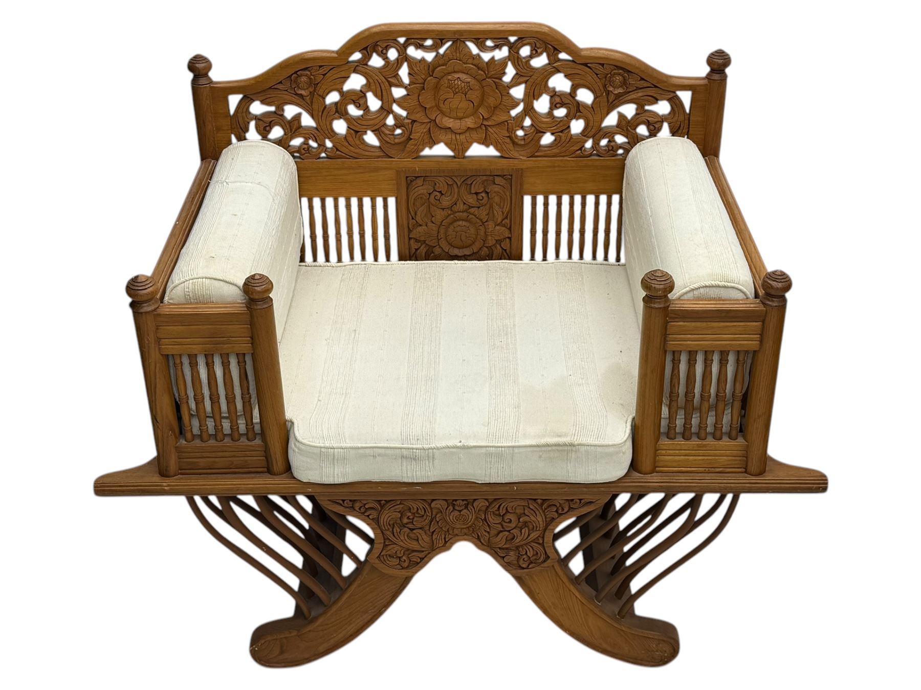 Early 20th century carved teak Howdah elephant chair, with pierced floral and foliate carved backrest, spindle gallery arm supports, cream upholstered cushions, splayed legs on a curved reeded base 