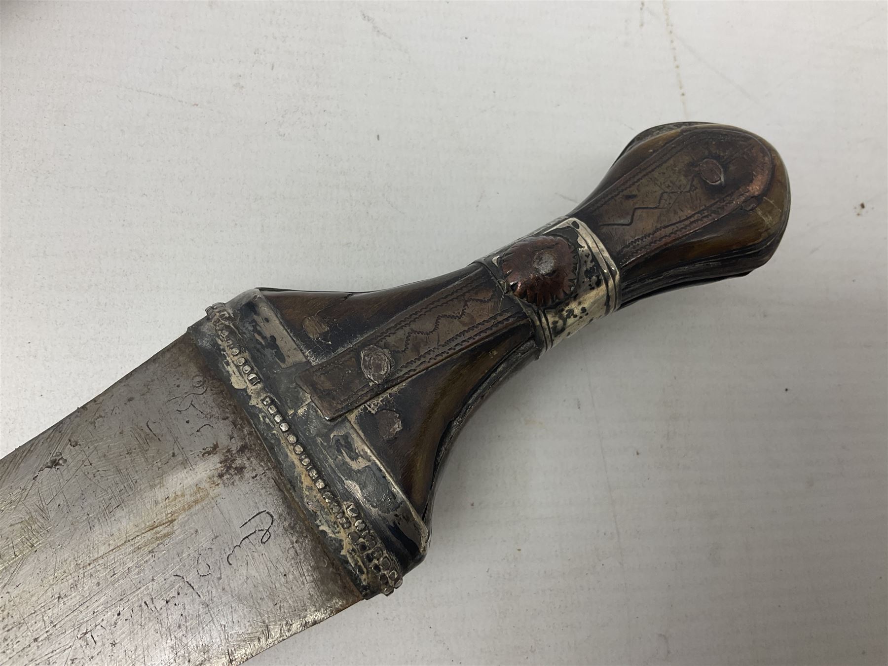 Late 19th/20th century Middle Eastern jambiya dagger the 36cm broad curved double edged steel blade with traces of script, horn and copper backed waisted white metal hilt with three roundel buttons; in ornate white metal and leather mounted brass and steel scabbard L60.5cm overall