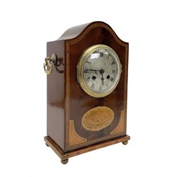 Edwardian- 8-day mantle clock in a mahogany case with a serpentine top and contrasting inlayed panels in satinwood and boxwood to the front, on a rectangular plinth raised on ball feet, silvered dial with Roman numerals and steel spade hands, twin train Parisian rack striking movement, sounding the hours and half hours on a coiled gong. With pendulum.