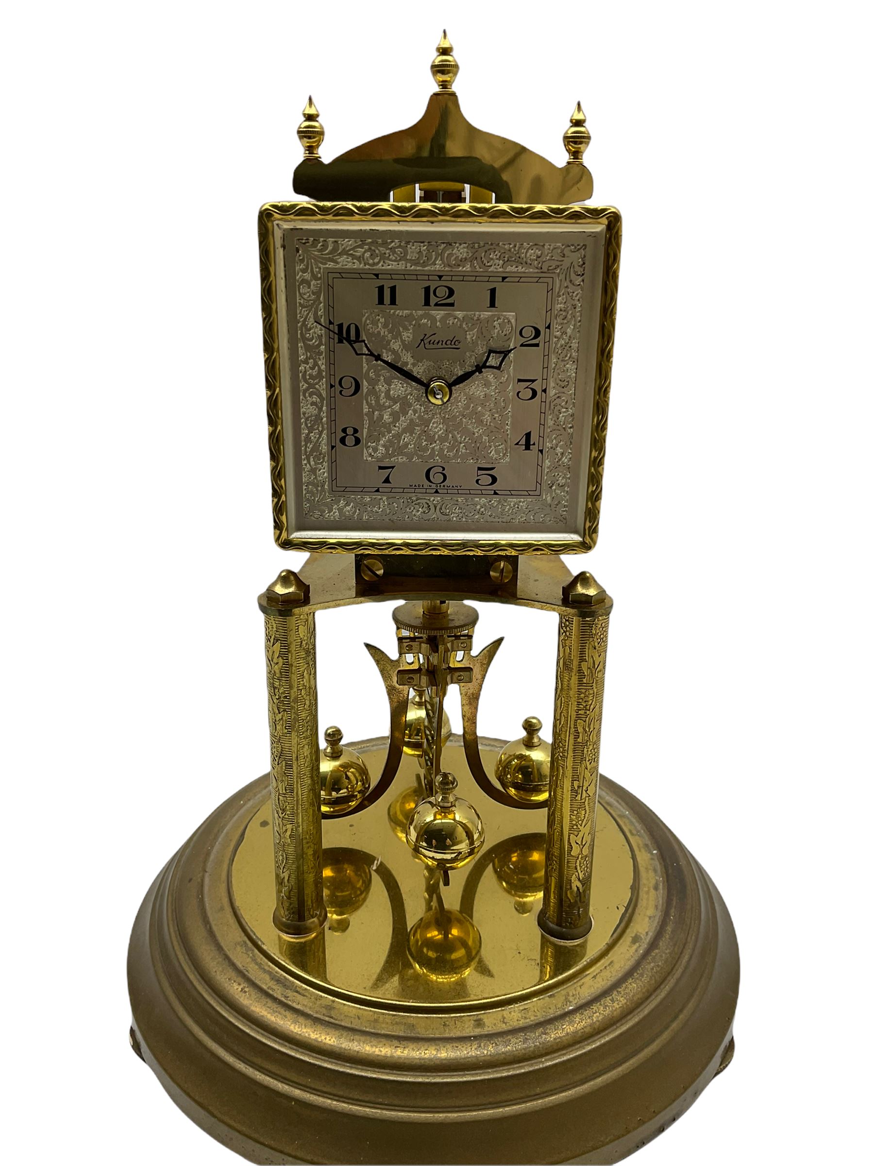 A “Kundo” 400-day torsion clock made by the 20th century German manufacturer Kieninger & Obergfell, with a  decorative square dial and pierced steel hands within a foliate bezel, on a circular base with adjustable feet, four-ball rotary pendulum under a glass shade. 
H30cm
