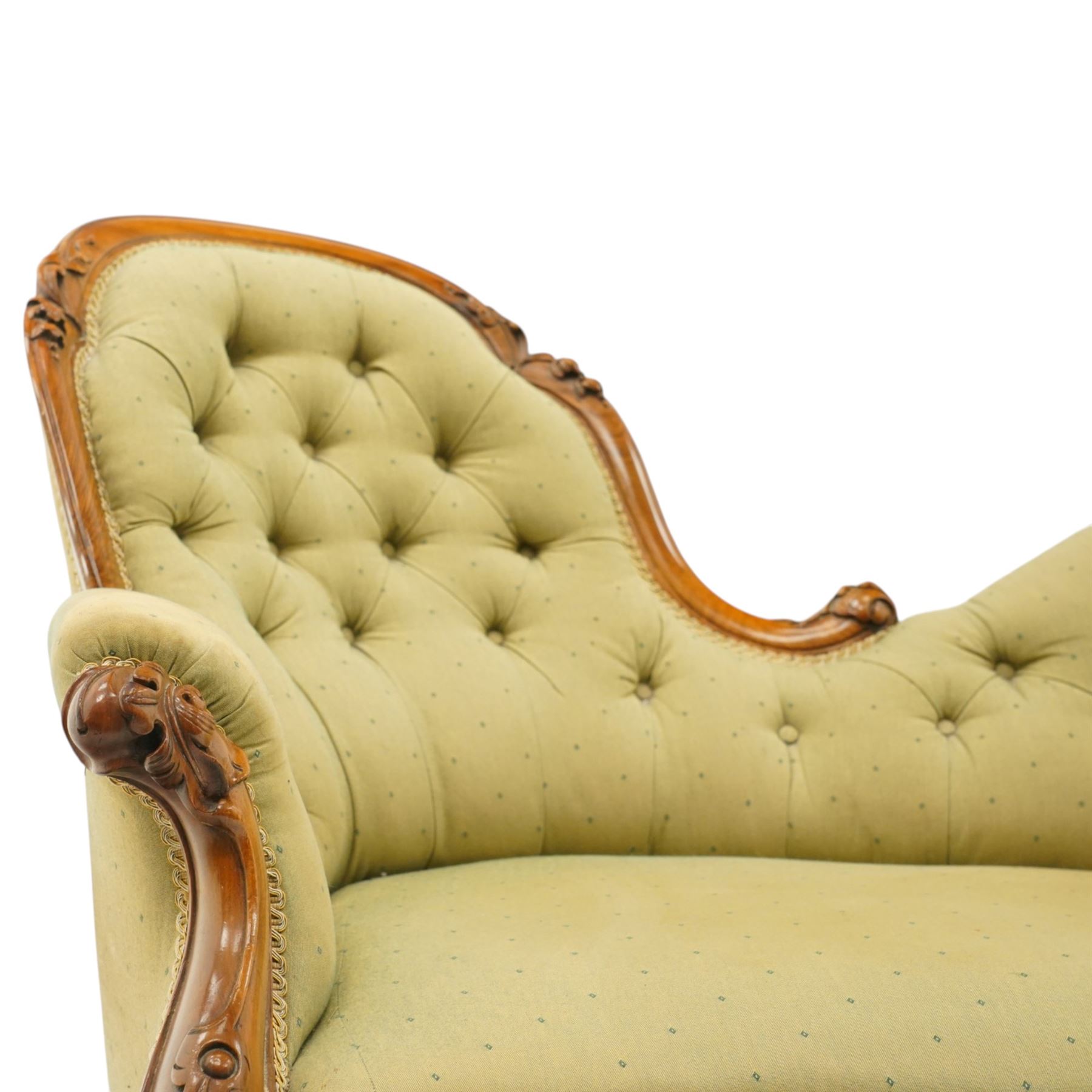 Victorian mahogany framed double ended chaise longue, serpentine button upholstered back with raised scrolled ends, padded arms and stuff-over seat upholstered in green fabric, carved showframe with foliate terminals and scroll supports, on short cabriole legs with brass castors