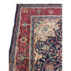 Persian Kashan red and blue ground carpet, the central floral rosette medallion surrounded by interlacing foliate branches and stylised plant motifs, flower head border guards and repeating scrolling main band