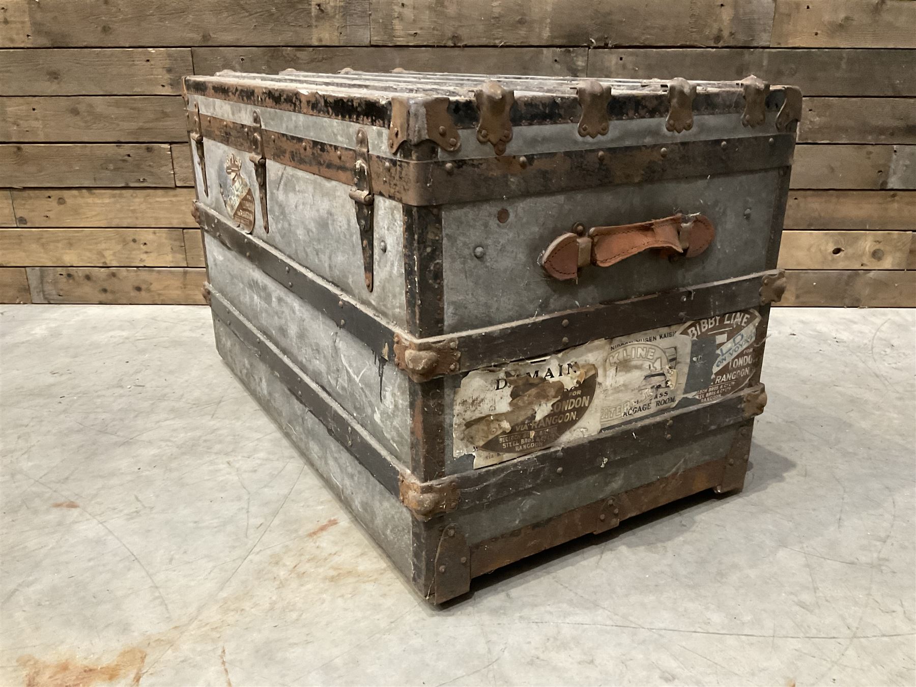 Early 20th century wood and metal bound zinc travelling trunk, hinged top with three clasps, decorated with period luggage labels