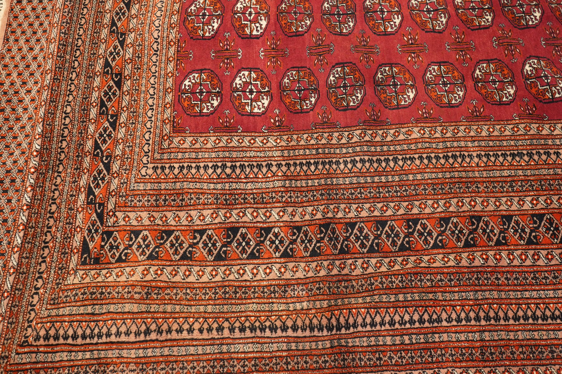 Large Afghan Bokhara crimson ground carpet, the field with rows of repeating Gul motifs and geometric design, enclosed by multiple repeating geometric guard bands