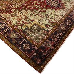 Northwestern Persian Heriz carpet, crimson ground and soft green field, with bold terracotta stepped medallion with angular spandrels and geometric motifs within a broad palmette and vine border 