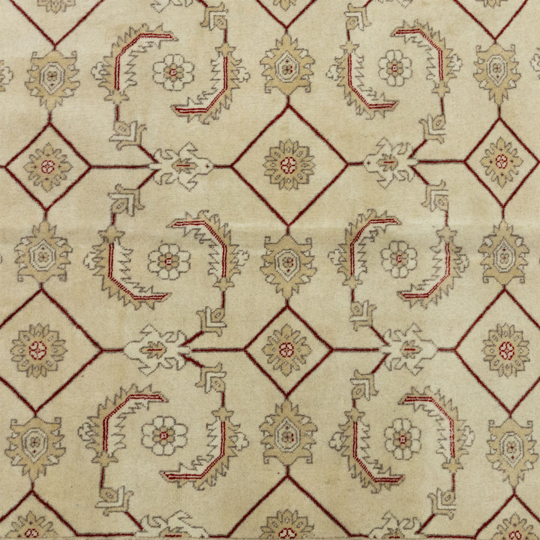 Baluchi signed hand-knotted rug, ivory ground, with an all-over geometric lattice design incorporating stylised flowerheads, hooked motifs and angular vine work, enclosed by a crimson border with repeating floral motifs and scrolling vines, flanked by narrow patterned guard stripes, signed to one corner, with cotton fringes