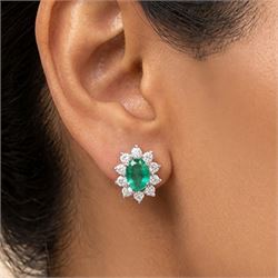 Pair of 18ct white gold emerald and diamond cluster earrings, each stud set with a single oval cut emerald surrounded by round brilliant cut diamonds, stamped, total emerald weight approx 0.75 carat, total diamond weight approx 0.55 carat