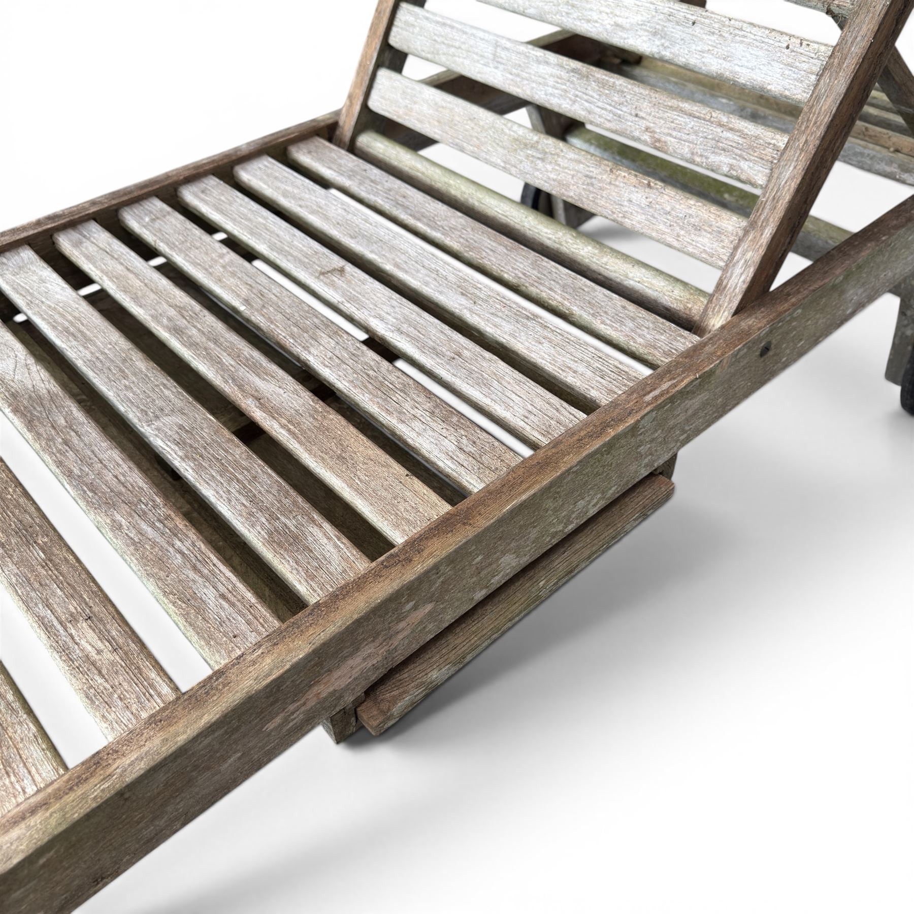 Pair of teak garden sun loungers, with slatted adjustable backrests, integrated wheels and sliding pull-out side trays, weathered natural finish.