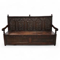18th century oak settle or bench, moulded cresting rail with globular finials over five panel back, each stepped arch panel carved with stylised leaf decoration, hinged box seat over S-scroll foliate frieze and two panels carved with scrolling pattern, panelled sides, on stile supports terminating to turned feet 