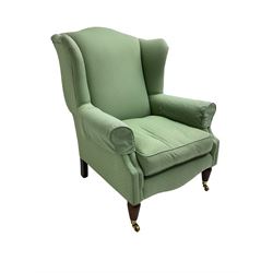 Wingback armchair, upholstered in light green fabric, on turned and fluted front feet with brass cups and castors