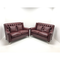 Pair Duresta two seat high back sofas upholstered in deep buttoned maroon leather, ebonised supports on chrome castors, W150cm