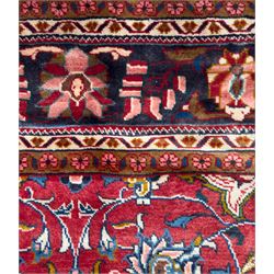 Northwestern Persian Lillihan hand-knotted carpet, madder red field with scrolling vines, rosettes, and palmettes around a central circular medallion in navy, ivory and ochre, and ivory ground spandrels within a navy border of stylized flowerheads and vines between multiple guard stripes 