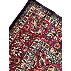 Persian Kashan indigo ground carpet, large central rosette medallion decorated with alternating palmettes, the surrounding field and spandrels with overall floral design depicting trailing branches and stylised plant motifs, crimson ground border with trailing floral pattern, enclosed within guard stripes 
