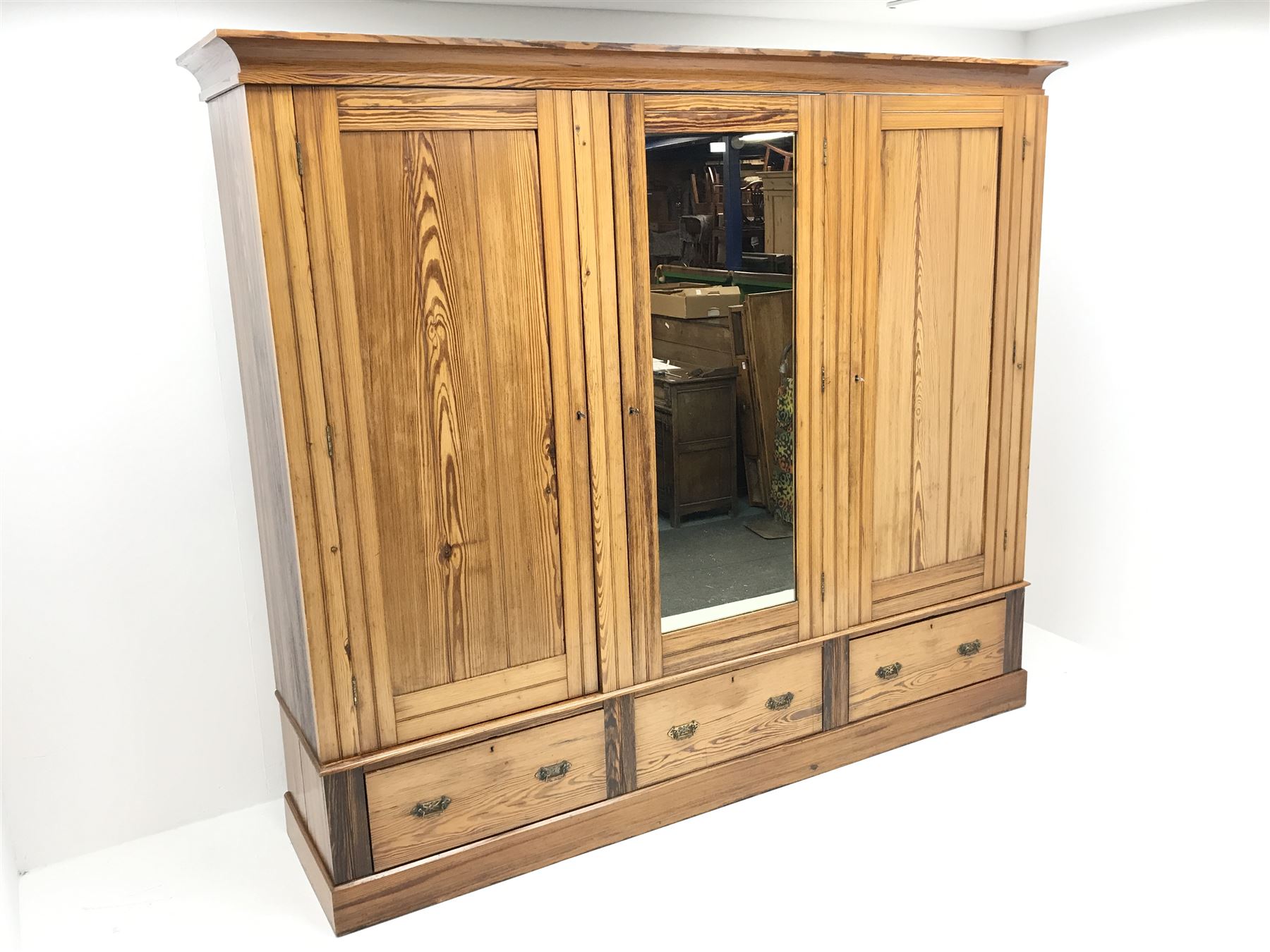 Late Victorian large pitch pine triple wardrobe, projecting cornice, central mirrored door flanked by two others above three drawers, plinth base