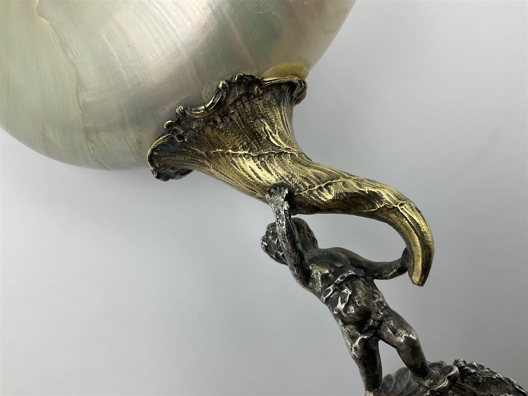 Modern limited edition silver mounted nautilus shell cup, no. 42/150, the pearlescent shell cup with silver-gilt strapwork to rim, upon a stem modelled as a putto supporting a gilt cornucopia and circular domed foot depicting Poseidon amongst swirling waves, hallmarked by St James House Company, London 1980,  H17.5cm