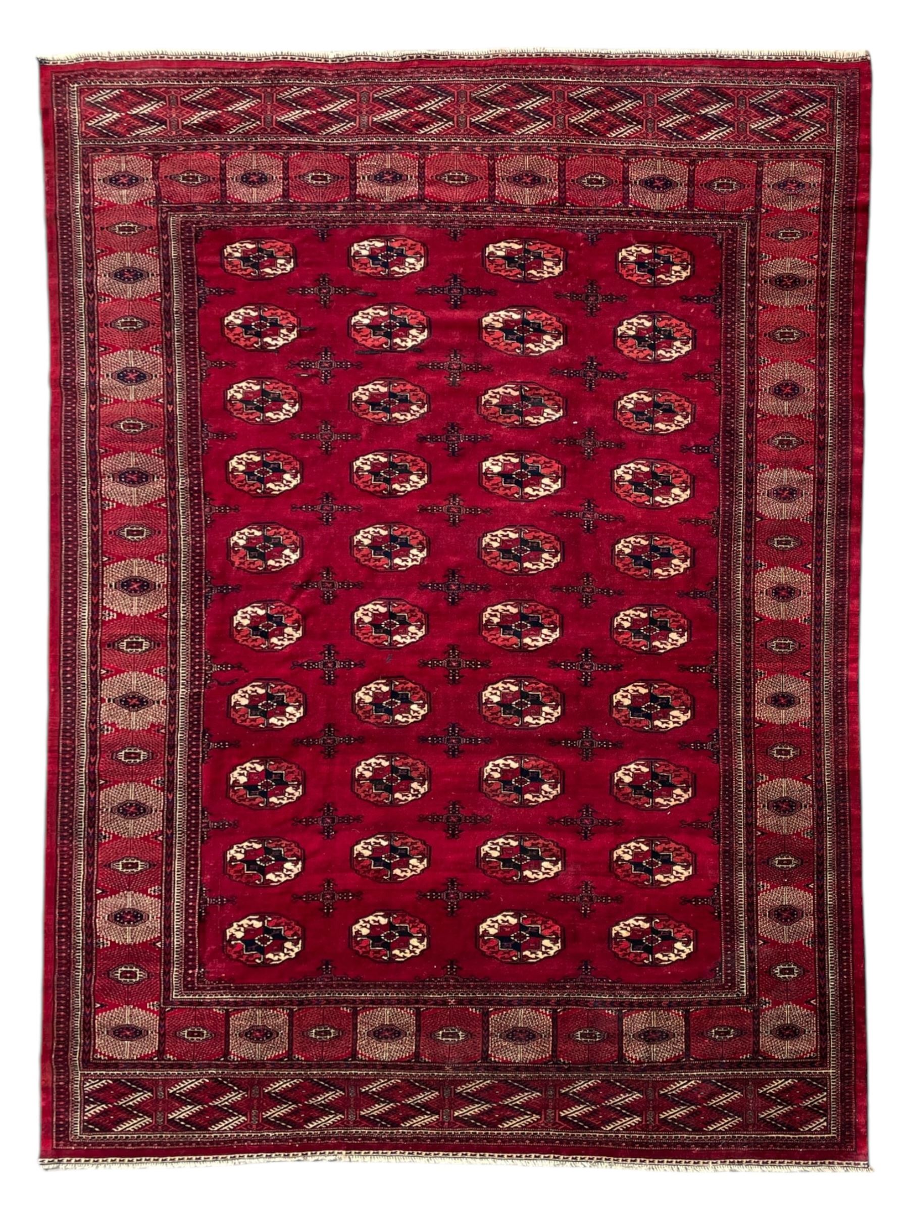 Afghan Bokhara red ground carpet, the field decorated with four rows of Gul motifs interspersed with Hac motifs, the border with lattice pattern panels within small geometric guard stripes, geometric patterned end panels