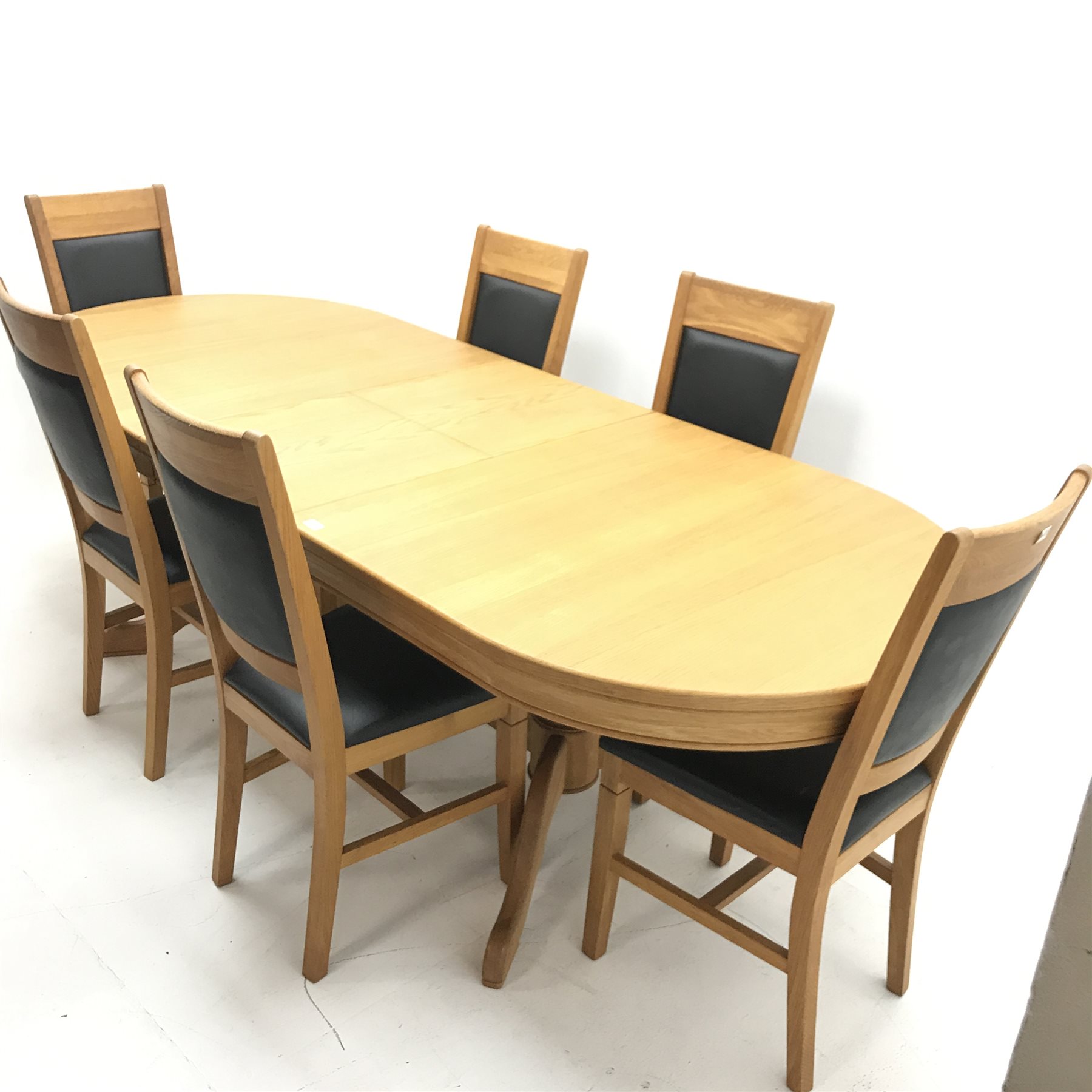 Oval solid oak extending dining table,  two turned columns on shaped supports joined by stretcher (W200cm and 250cm, H68cm, D101cm) and six oak framed chairs, upholstered back and seat (W44cm)