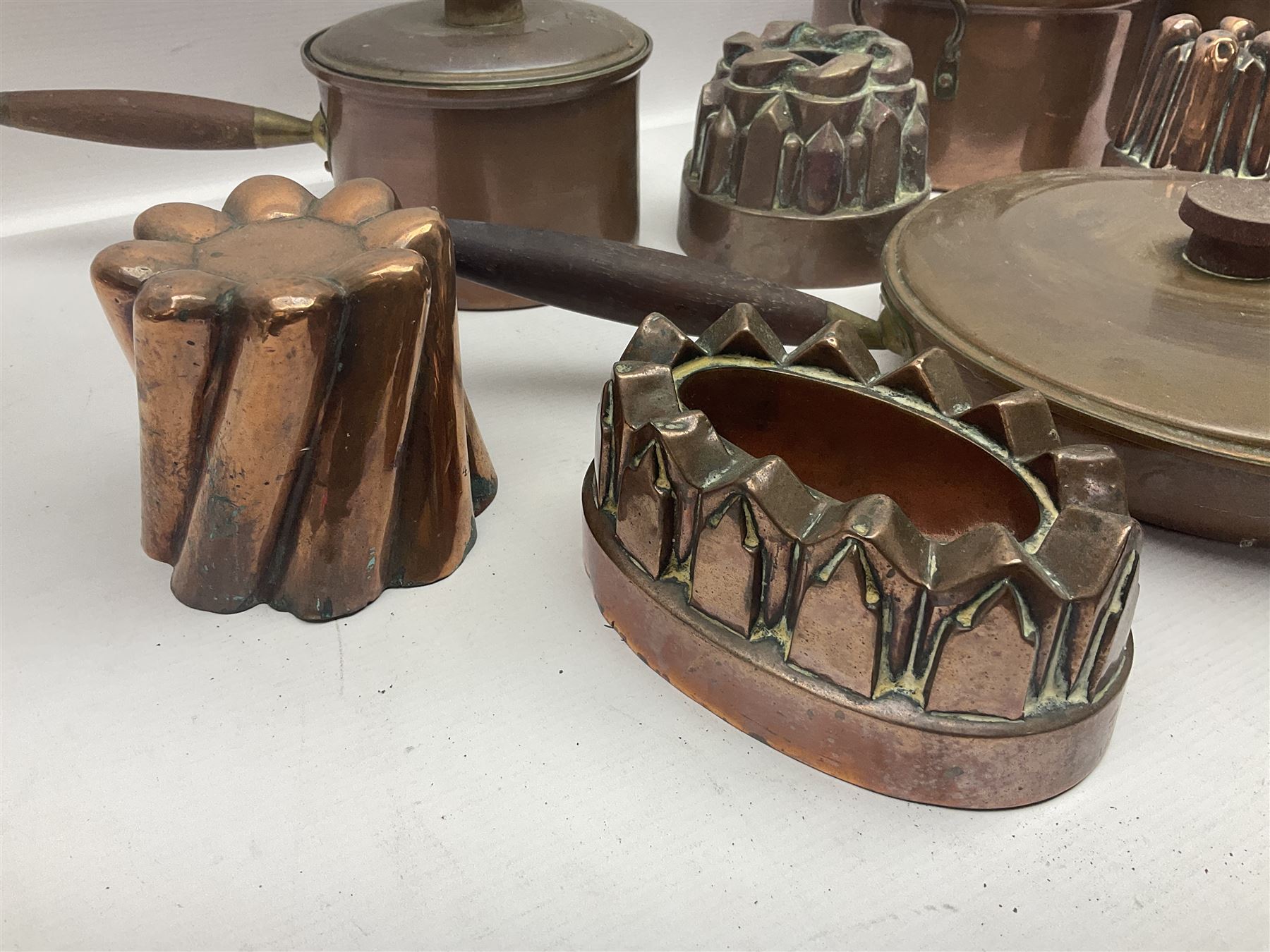 Four Victorian copper moulds, together with a graduating set of copper pans with wooden handles and finials to covers, largest pan 