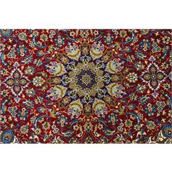 Fine Central Persian Isfahan hand-knotted rug, madder red field with central finely drawn foliate medallion issuing an intricate all-over scrolling vine design with palmettes and arabesques, enclosed by multiple conforming borders in navy ground, signed Isfahan in cartouche, silk fringe ends 
