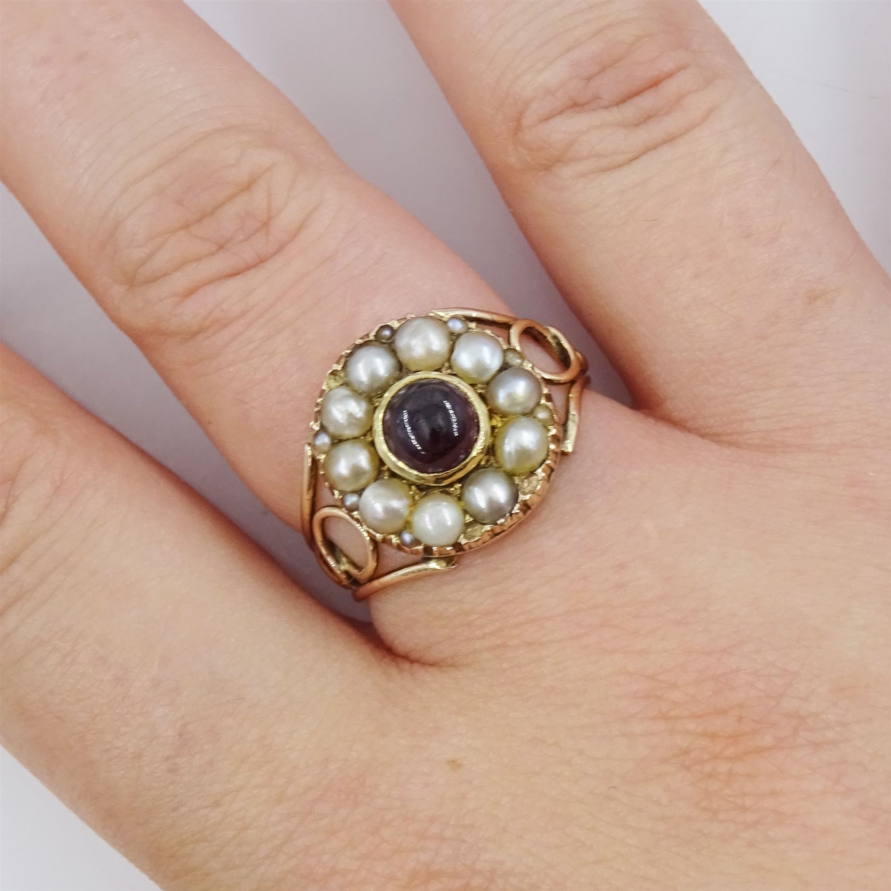 George III 9ct rose gold garnet and pearl mourning ring, single cabochon garnet, with split and seed pearl surround and pierced design shoulders, the back inscribed and dated 1808