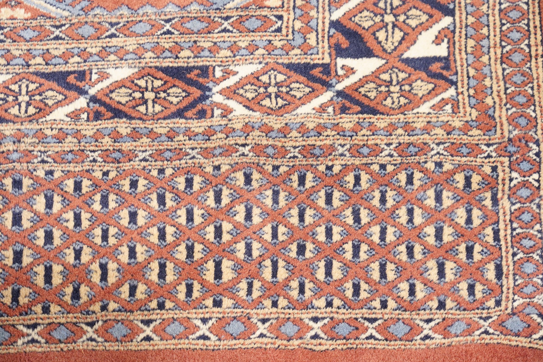 Afghan Turkoman crimson ground rug decorated with twin rows of hooked geometric guls within broad compartmented geometric borders (125cm x 201cm); Afghan Bokhara rug with repeated octagonal guls on a terracotta ground, enclosed by multiple geometric borders and patterned elem panels (120cm x 192cm) (2)