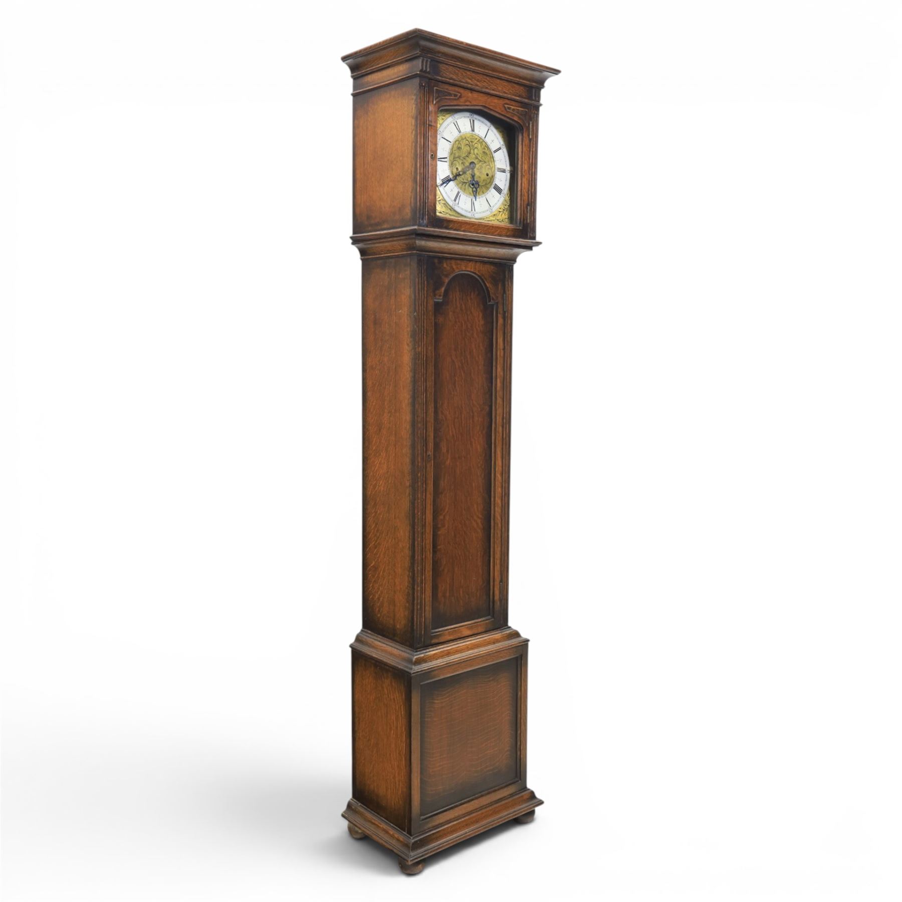 Early 20th century oak longcase clock, square brass dial with engraved foliate spandrels and centre, silvered Roman chapter ring with Arabic minute track, Westminster chime movement, the plain case with glazed arched trunk door and moulded plinth