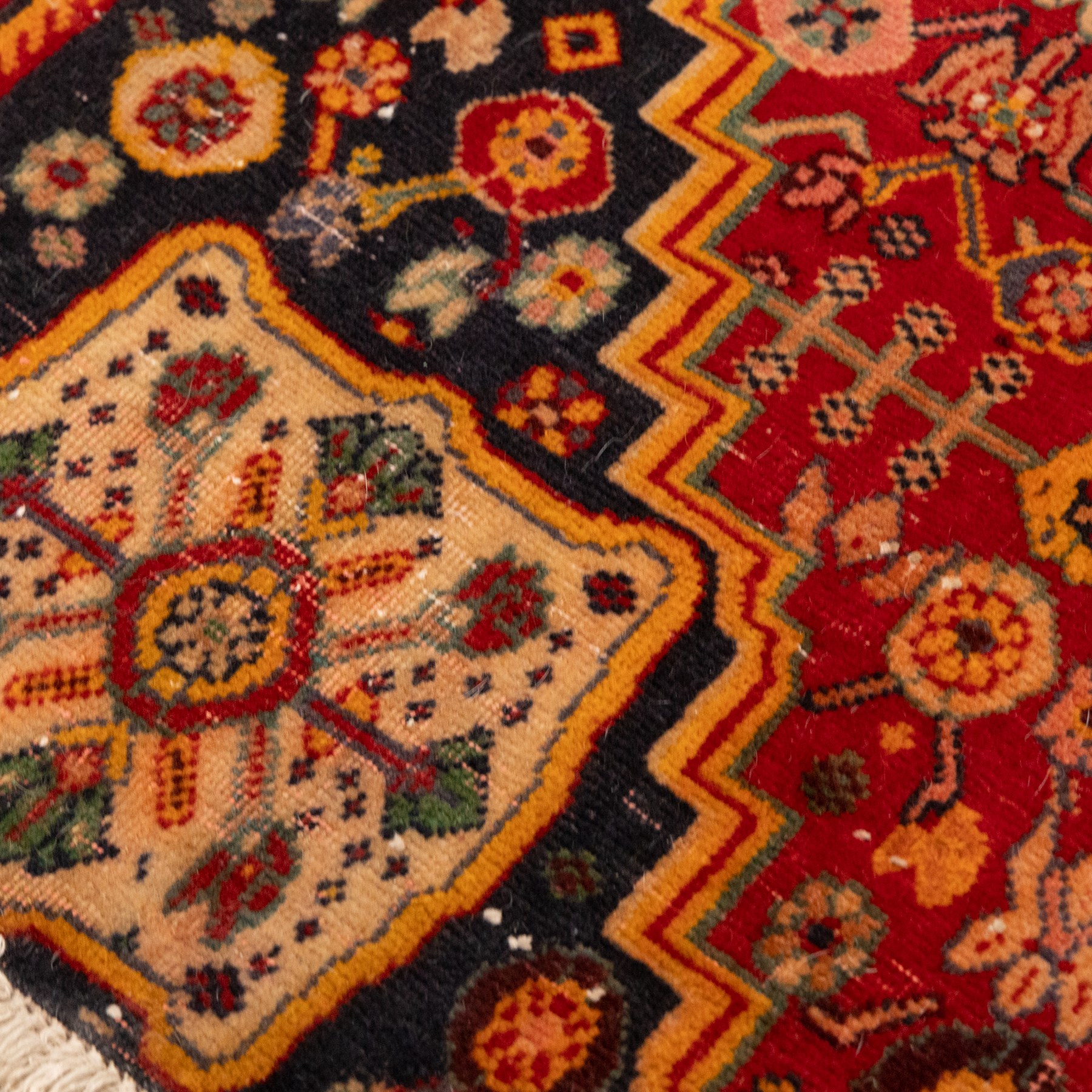 North Persian crimson ground rug, the field densely decorated with stylised flowering plants, urns and polychrome rosettes, within a stepped ochre outline, dark ground floral spandrels and geometric side panels